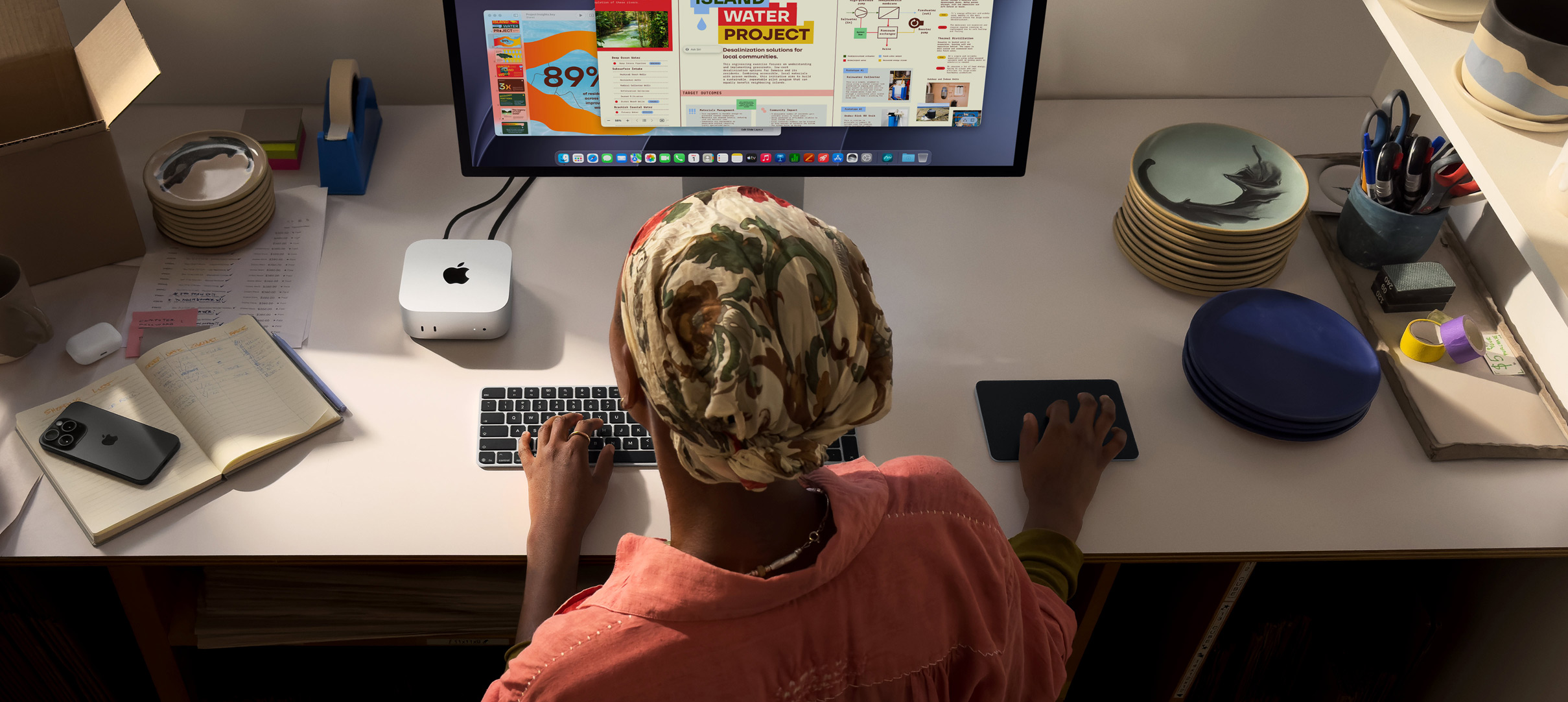 Eine Person tippt an einem Schreibtisch mit einem Mac mini, Studio Display angeschlossen, Magic Keyboard, Magic Trackpad, verschiedene Objekte