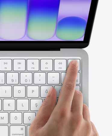MacBook Neo, gümüş rengi, kullanıcının parmağı klavyenin sağ üst köşesindeki Touch ID sensörüne dokunuyor