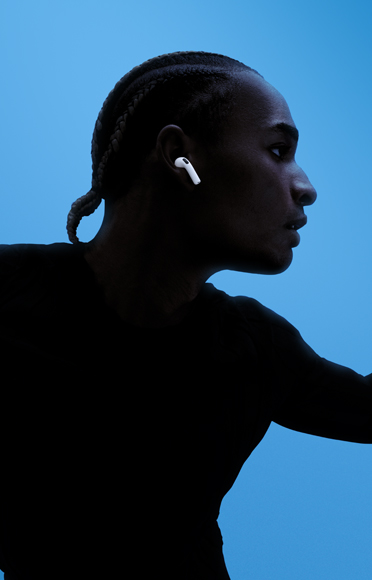 Une personne portant des AirPods 5, bras grands ouverts, sur un fond coloré