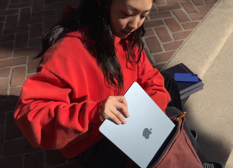Una persona sentada en unos escalones de piedra que coloca su MacBook en una mochila.