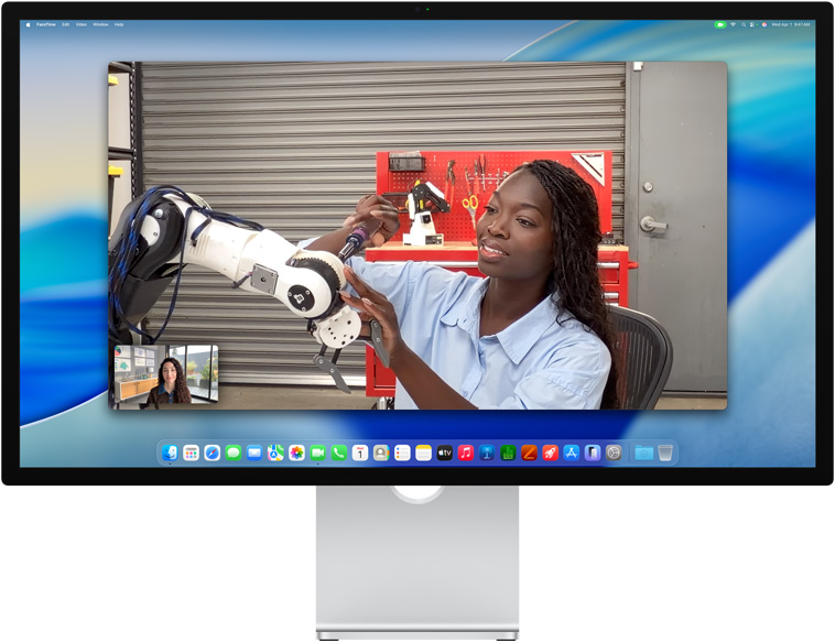 Dos personas en una videollamada en un monitor Studio Display, Encuadre Centrado las mantiene en el centro de la imagen incluso cuando una de ellas se mueve para reparar un equipo
